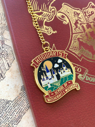 Harry Potter bookmark featuring colorful , round charm of illustrated Hogwarts castle, shown on gold chain, displayed on red notebook with gold HP crest.