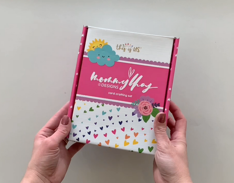 Female hands pick up and show in detail the contents of this "Mommy Lhey" card-making craft kit.