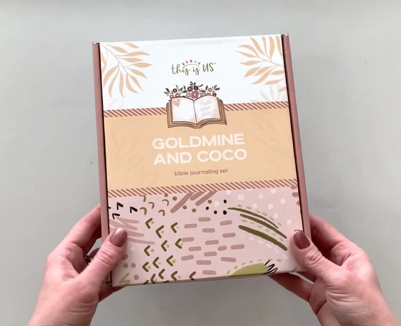 Female hands picks up box and show all the contents of this Goldmine And Coco Bible Journaling craft kit.