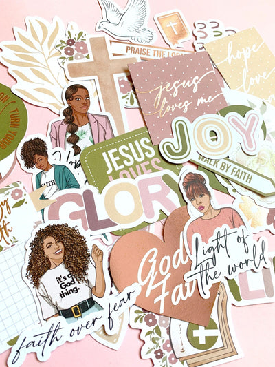 An assortment of die cut stickers from this bible journaling craft kit are displayed overlapping, featuring patterns, illustrations and spiritual sayings depicted in beautiful soft, muted colors.