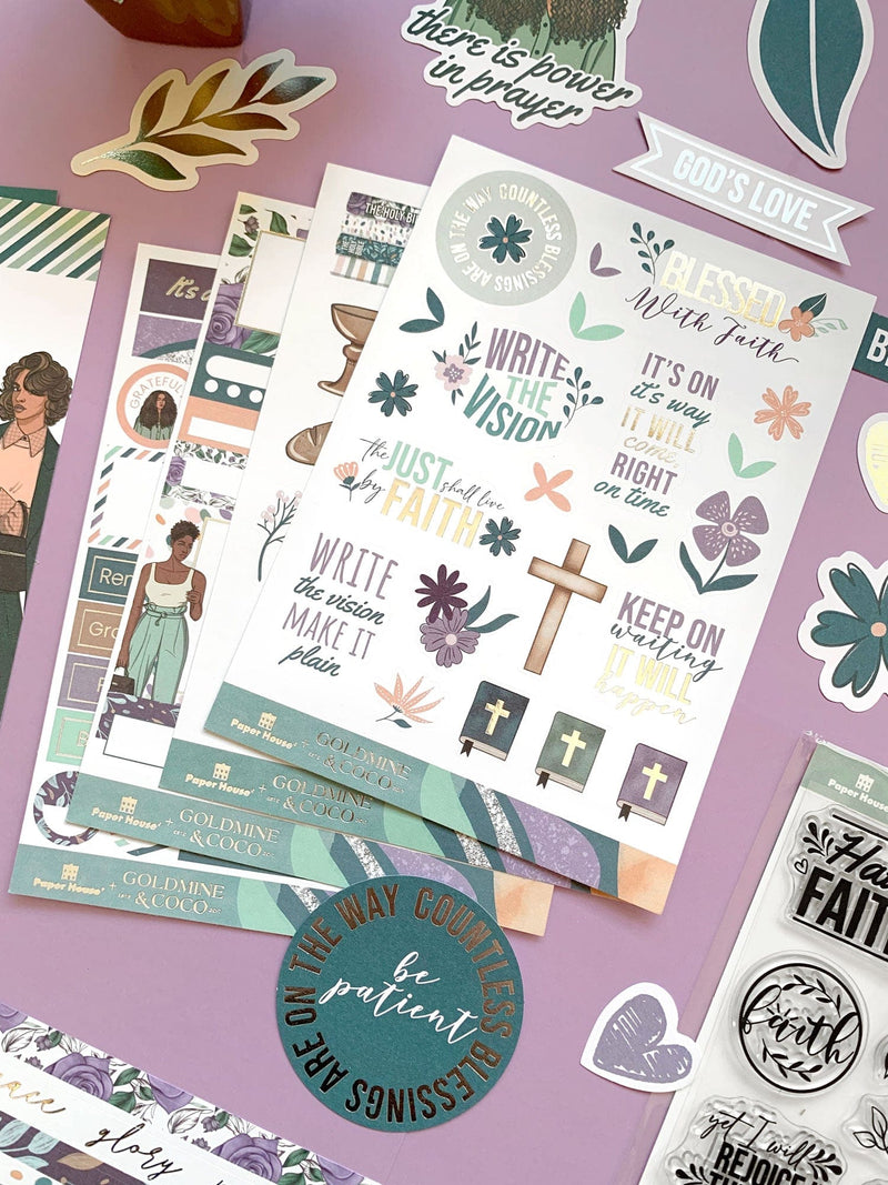 An assortment of craft kit components including papers, stickers and die cuts featuring teal and purple patterns, hearts, crosses and flowers are shown on a purple background.
