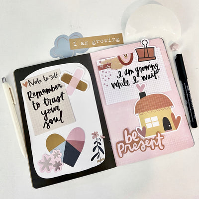 Soul care journal spread in pink, black, white, and gold color scheme with color block heart, cute house die cut, and handwritten notes: remember to trust your soul, and I am growing while I wait. 