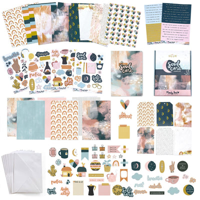 An assortment of craft kit components including papers, stickers, die cuts and envelopes featuring navy, gold and pink patterns and illustrations.