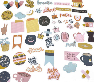 An assortment of craft kit die cut ephemera are shown on a white background, featuring navy, gold and pink illustrations and self care sentiments.