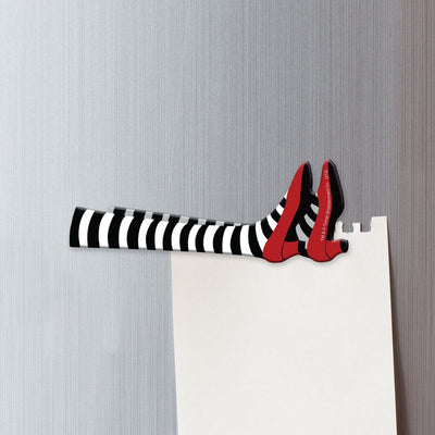 fridge magnet featuring the legs in black and white striped socks and red slippers of the Wicked Witch of the East shown on a metal background attached to a white sheet of torn memo paper.