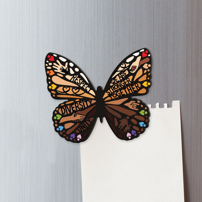 fridge magnet featuring a shaped, colorful, illustrated butterfly featuring words of diversity shown on a metal background attached to a torn sheet of memo paper.