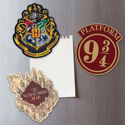 Three Harry Potter shaped magnets featuring the Hogwarts crest, the Marauder's Map and Platform 9 3/4 are shown on a metal background holding a white memo sheet.