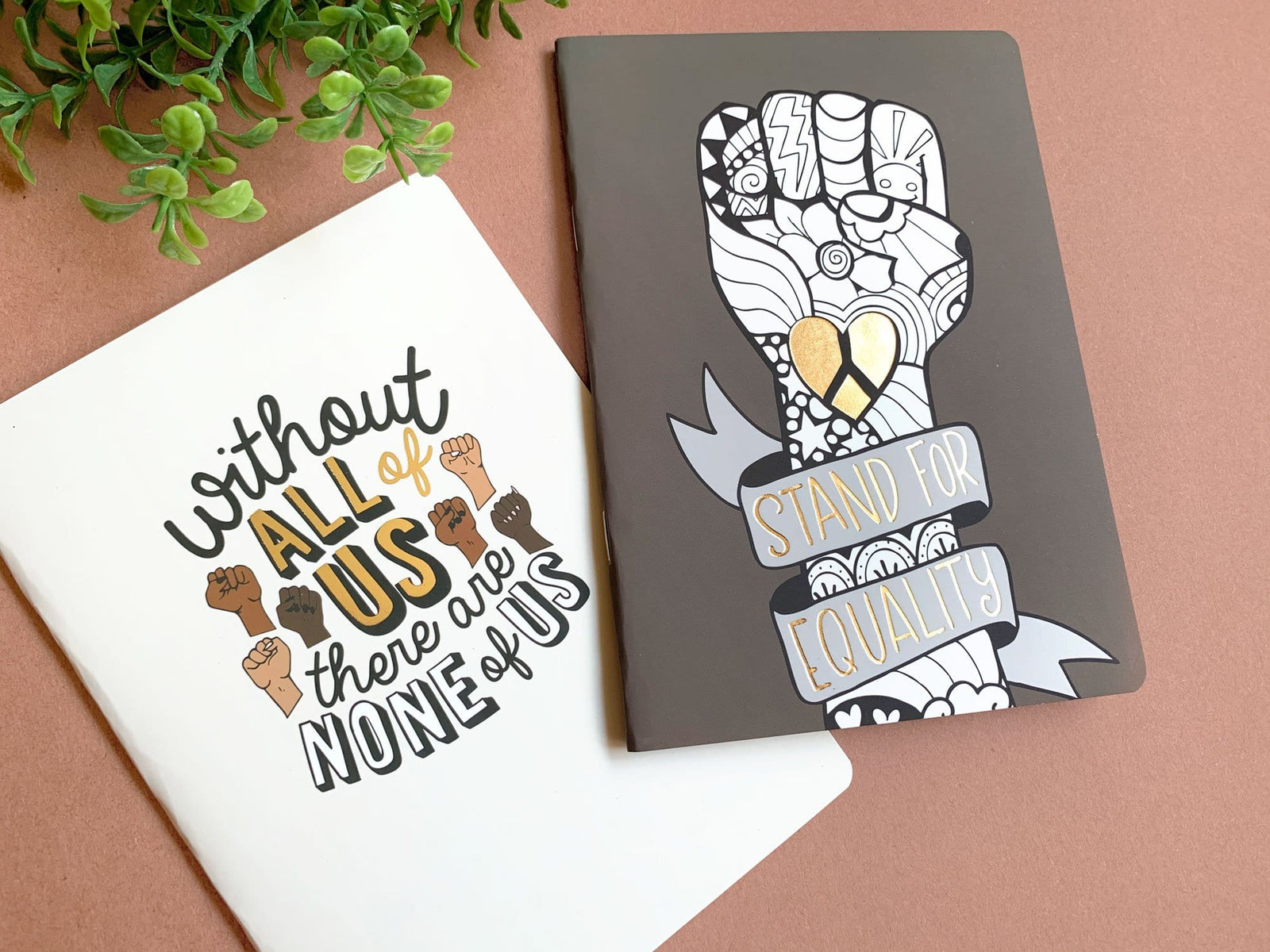 journal notebook set shown overlapping featuring "equality" depicted in black and white graphic illustration with gold details.