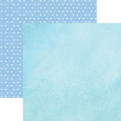 Double sided scrapbook paper featuring a blue watercolor pattern. Shown in front of a teal and white heart pattern on blue.