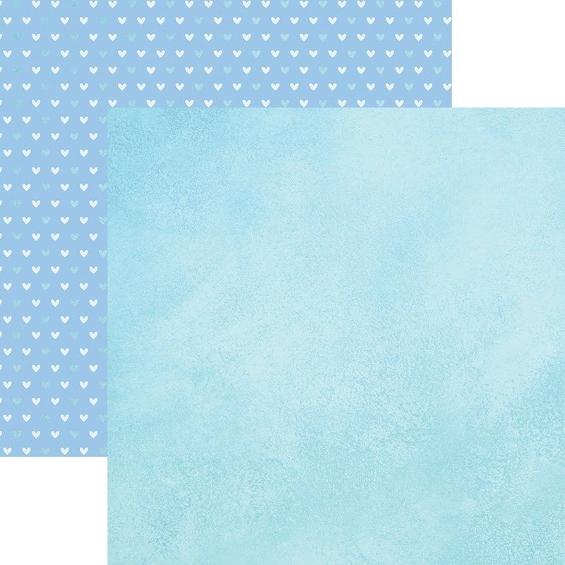 Double sided scrapbook paper featuring a blue watercolor pattern. Shown in front of a teal and white heart pattern on blue.