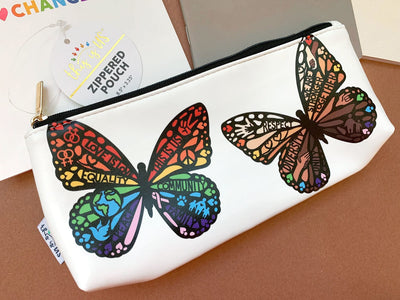 White pencil pouch with gold zipper featuring two colorful, illustrated rainbows with words of inspiration and inclusion shown on brown background.
