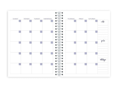 weekly planner featuring monthly spread with silver coil spine, shown on white background.