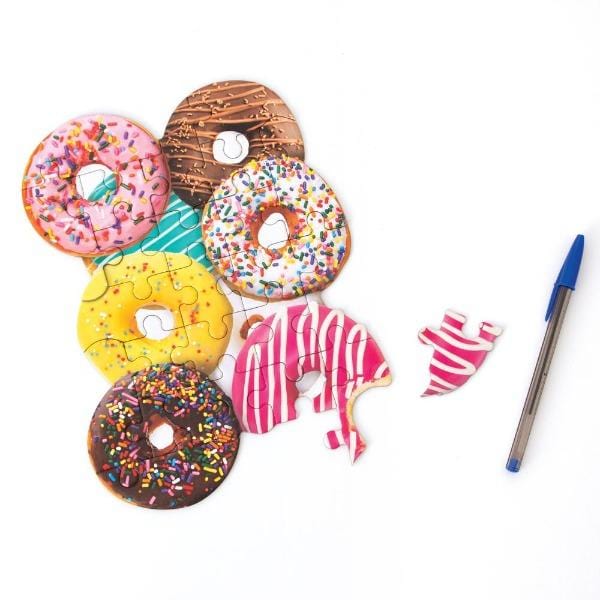 die cut mini jigsaw puzzle featuring photo real donuts, shown with pen and one piece removed, on white background.