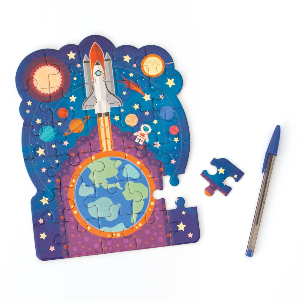 mini die cut jigsaw puzzle featuring an illustrated rocket ship with planets, shown with pen and a separate puzzle piece on white background.