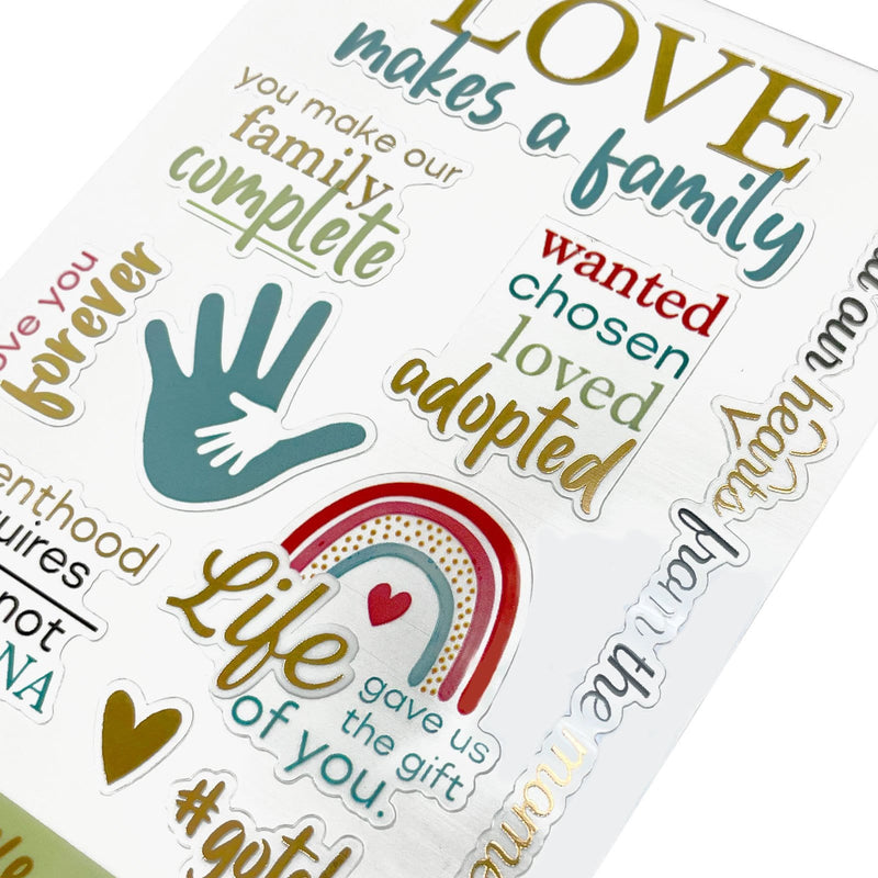 This image of scrapbook stickers shows the adoption themed sticker sheet on an angle featuring sentiments of love with gold, teal and red details.
