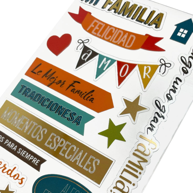 This image of scrapbook stickers shows the spanish family themed sticker sheet on an angle featuring sentiments of love with orange and gold details.