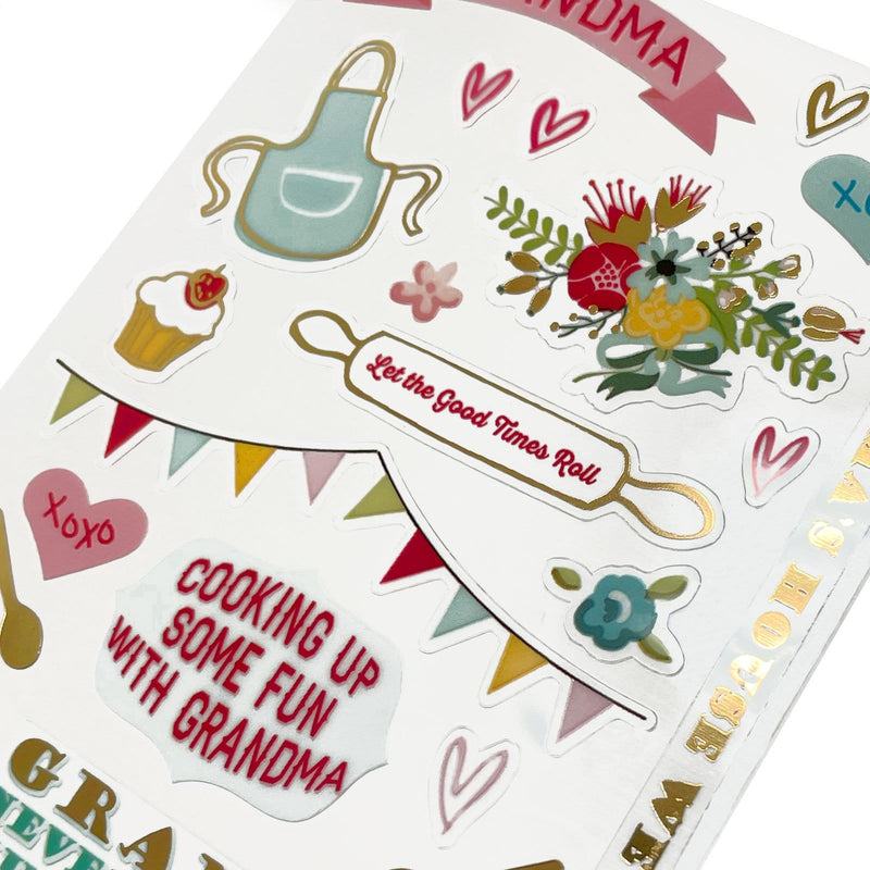 This image of scrapbook stickers shows the grandma themed sticker sheet on an angle featuring sentiments of love with pink and gold details.
