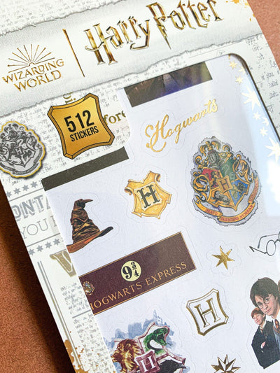 close up of Harry Potter sticker book featuring crests, sorting hat, harry and ron, shown in package on brown background.