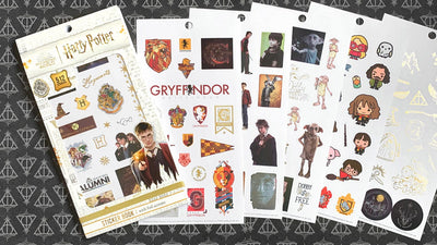 Six pages of planner stickers from the Harry Potter sticker book fanned out  over  black and white horcrux scrapbook paper