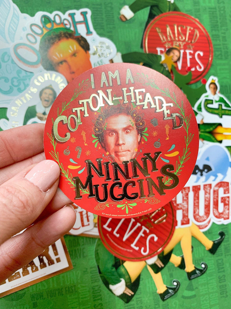 close up of scrapbook sticker featuring a round die cut of Buddy The Elf displayed in hand, shown above an assortment of Buddy stickers on green background.