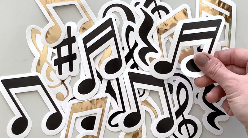 hand displays an assortment of black and gold die cut, musical note scrapbook stickers.
