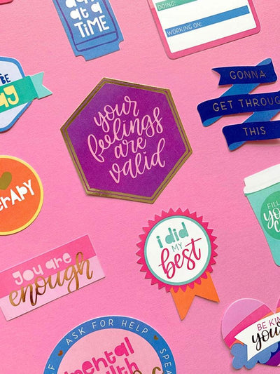 close up of scrapbook stickers featuring die cut stickers with colorful, positive sentiments, shown on pink background.