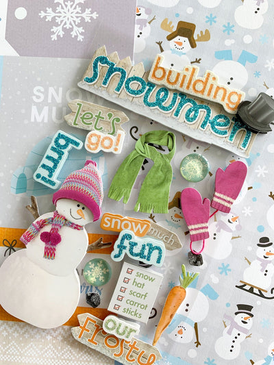 colorful 3D scrapbook stickers featuring a snowman wearing a pink hat and scarf, "Building Snowmen" title sticker, and other snomman accessories