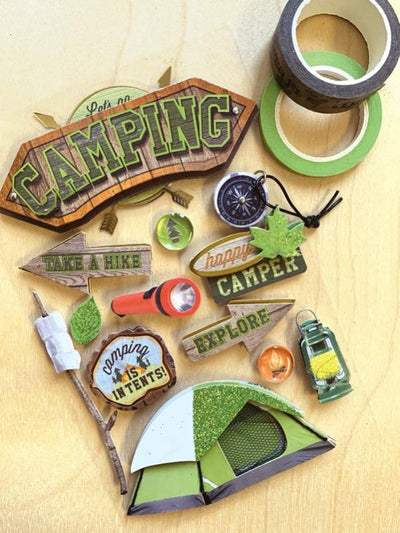 3D scrapbook stickers featuring a tent, marshmallows and a compass shown next to 2 rolls of washi tape on a wood surface.