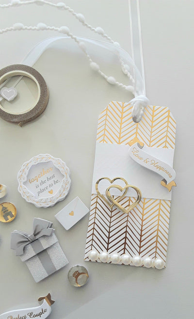 White and gold gift tag with two 3D stickers: love and happiness, and interlocking gold hearts. Pearl accents along the bottom.