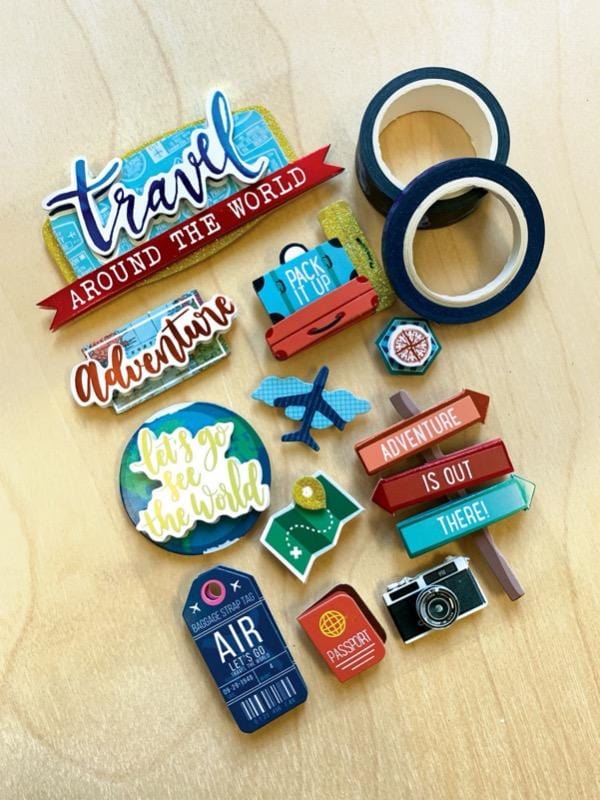 3D scrapbook sticker featuring colorful illustrations of airplane, camera and luggage shown next to 2 rolls of washi tape on a wood surface.