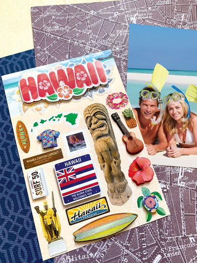 scrapbook stickers featuring Hawaii with hibiscus flowers and the state flag shown next to a photo of a couple snorkeling at the beach on a background of patterned papers.