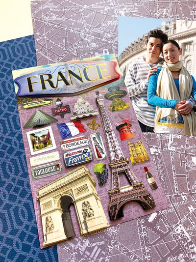 3D scrapbook stickers featuring the eiffel tower and the arc de triomphe shown next to a photo of a young couple on a patterned background.
