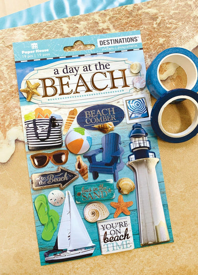 3D scrapbook stickers featuring photo-real lighthouse, sailboat and shells shown next to 2 rolls of washi tape on a patterned sand background.