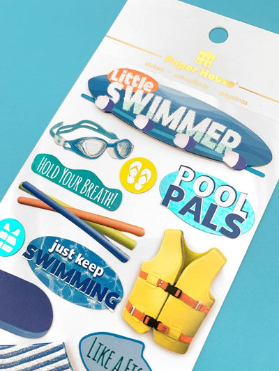 Scrapbook sticker featuring words, goggles, flip flops and pool noodles. Blue, yellow and orange with clear glitter and teal foil details. Shown in white package with gold foil letters on teal background.