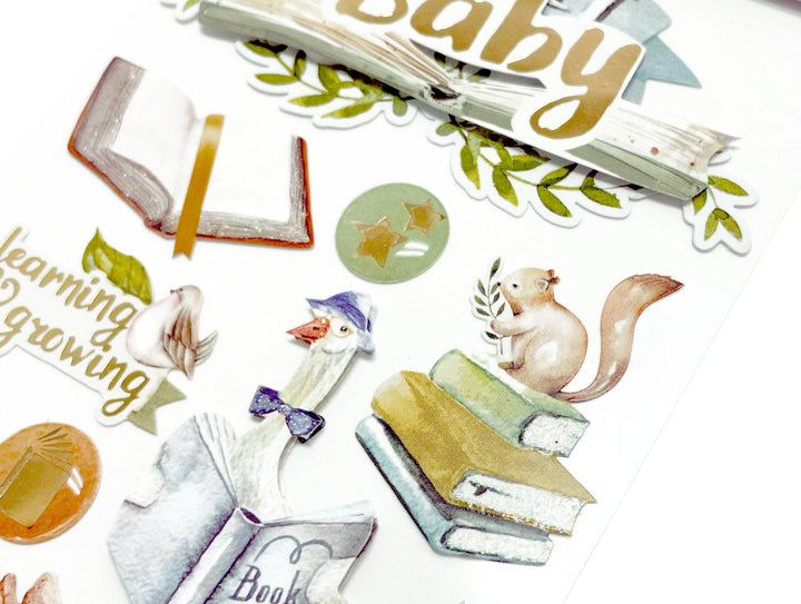 Close up of baby themed scrapbook stickers featuring mother goose and gold details.