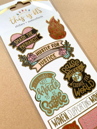 close up of foil stickers featuring Hustle for Justice sentiments with gold details, shown in package on tan background.