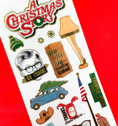 close up of foil stickers featuring "A Christmas Story" scenes, illustrated and embellished in gold foil, shown on red background.