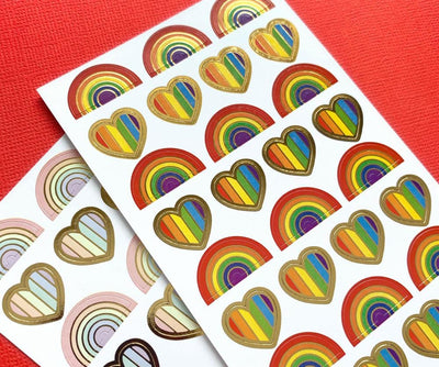 close up of planner stickers featuring bright colored and pastel rainbows and hearts with gold foil, shown on red background.