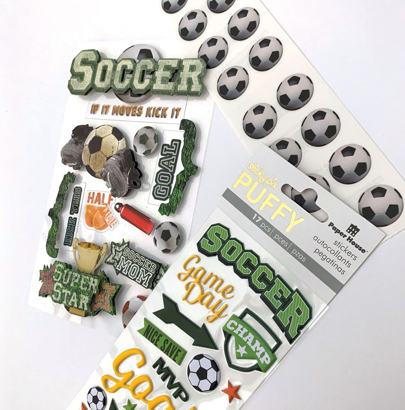 An assortment of soccer scrapbook stickers featuring words, uniforms, cones and soccer balls with silver foil shown layered on a white background.