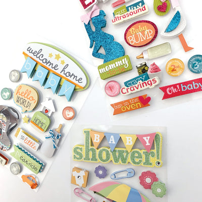 An assortment of scrapbook stickers featuring baby shower, bathtime, we're expecting, welcome home and sleeping baby with clear glitter details shown displayed on a white background.
