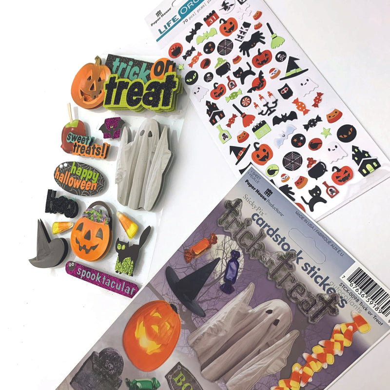 An assortment of halloween themed scrapbook stickers featuring pumpkins, haunted house and trick or treat with glitter and foil details shown layered on a white background.