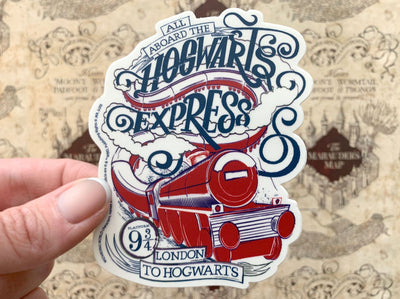 close up of shaped Harry Potter laptop sticker featuring an illustrated Hogwarts Express graphic in blue and red is shown being held in a hand against a map of the marauder's map background.