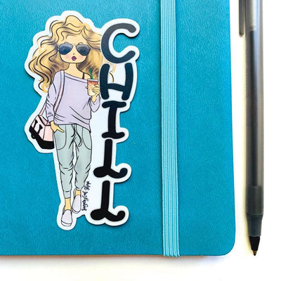 Shaped laptop sticker featuring an illustration of a blonde Lady D with the black letters CHILL stacked beside her, shown on a blue notebook with an elastic band and a ballpoint pen beside it.