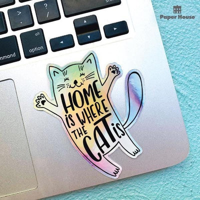 Shaped laptop sticker featuring a holographic illustrated cat with the words "Home is where the Cat is", shown on a laptop computer.