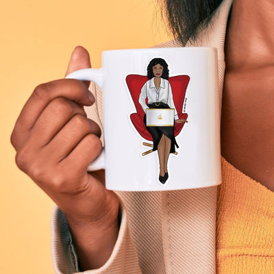 Shaped, vinyl sticker featuring a woman of color sitting in a red chair with a laptop, shown on a white mug held by a woman of color.