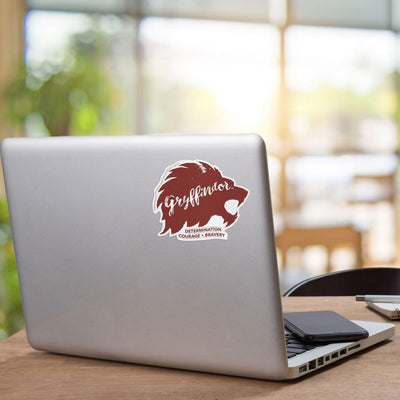 Shaped, vinyl sticker featuring words Gryffindor,  determination, courage and bravery. Deep red on white. Shown on laptop.
