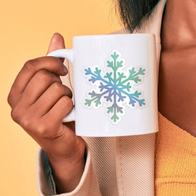 Snowflake Holographic Vinyl Laptop Sticker shown on a white mug held by a person.