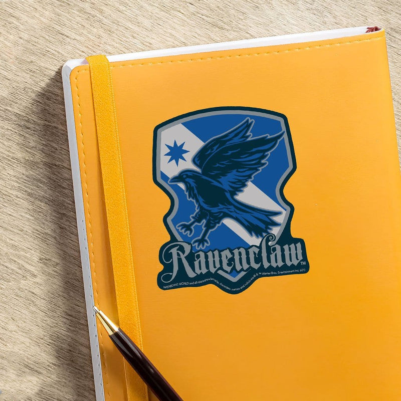 vinyl laptop sticker featuring Harry Potter Ravenclaw Shield shown adhered to orange notebook with pen.
