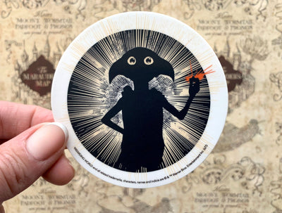 close up of vinyl laptop sticker featuring a Dobby Snap illustration in a circle, held in hand over a marauder's map pattern.