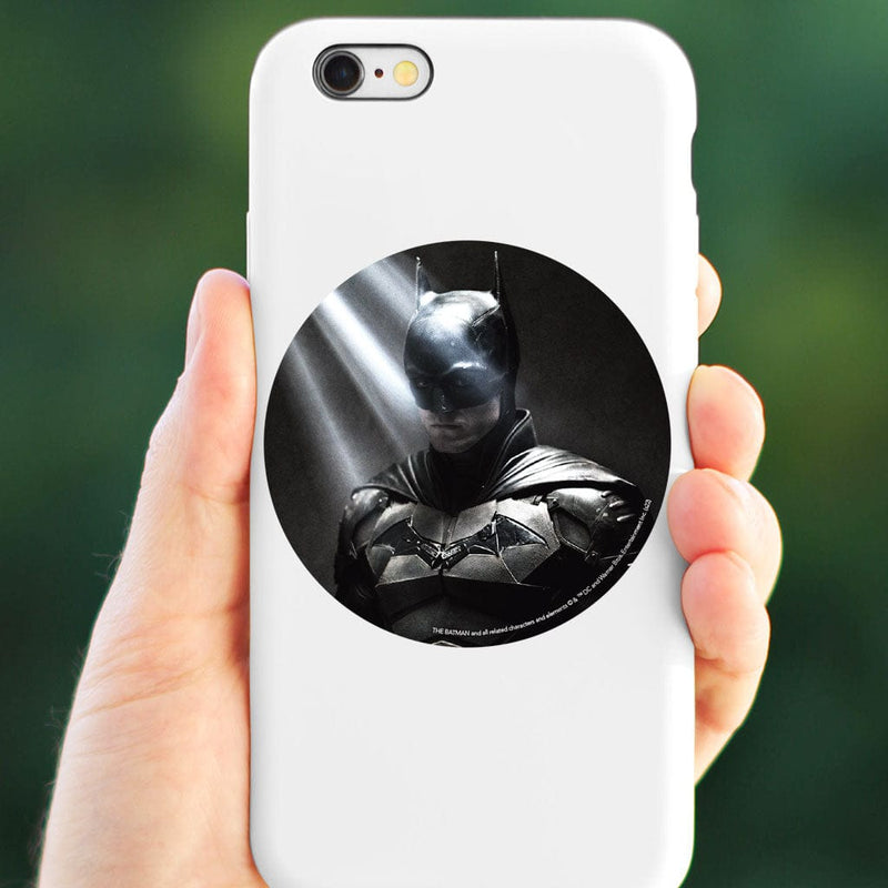 round vinyl sticker featuring a portrait of Batman in the light placed on a white cell phone, held in hand against a green background.